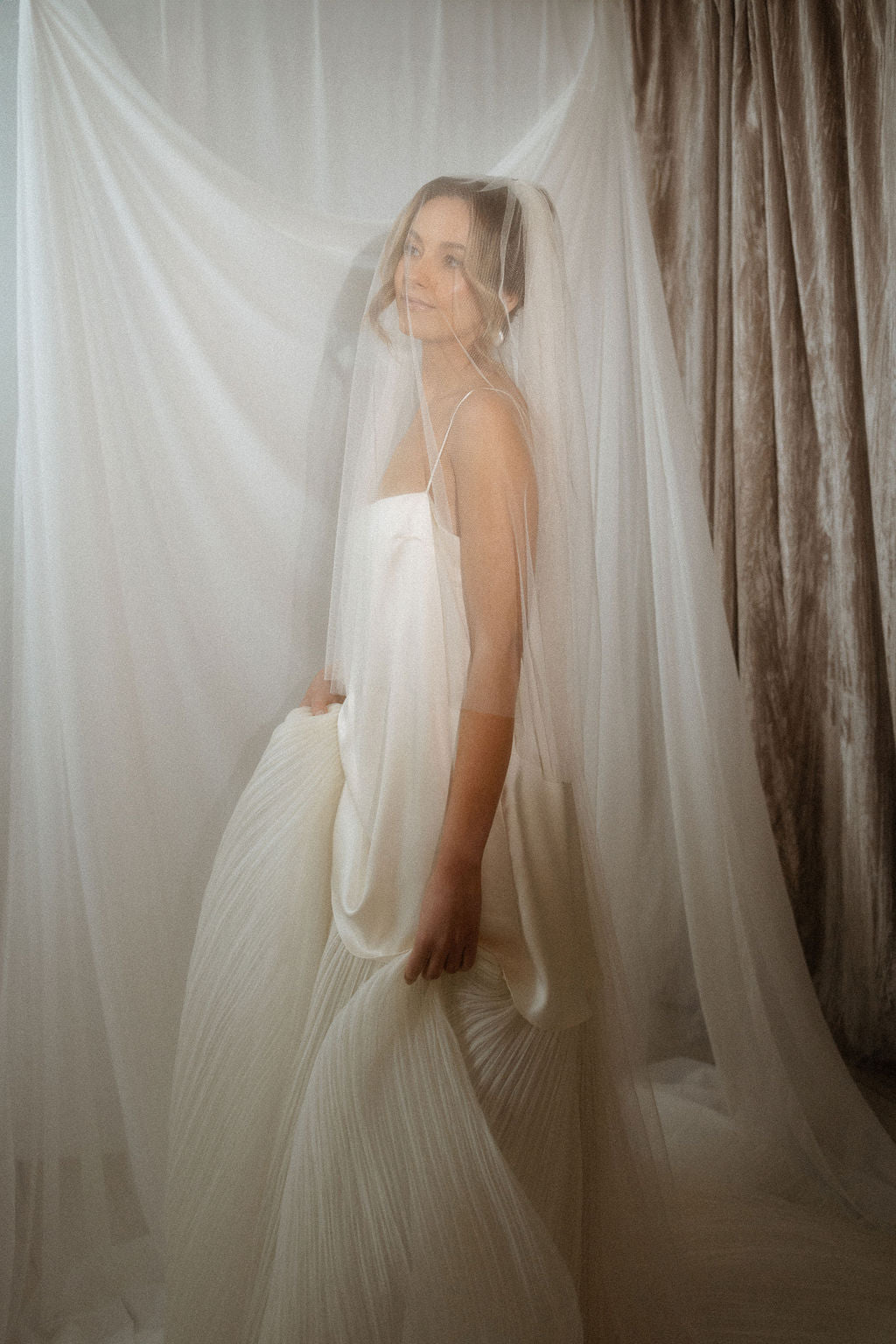 Woman in a white wedding dress standing in front of draped fabric