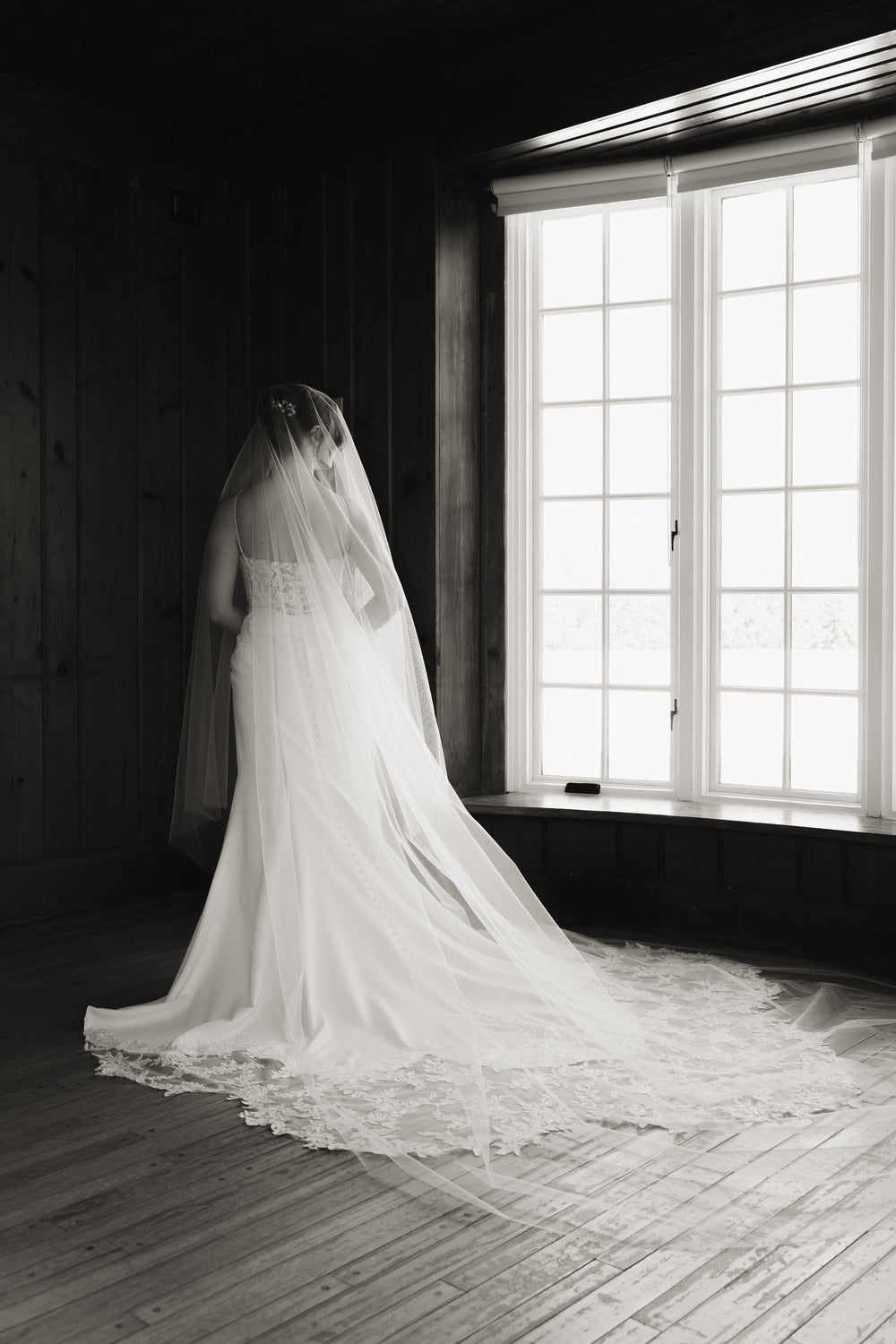Person wearing a long wedding veil standing in front of large windows with a scenic view.