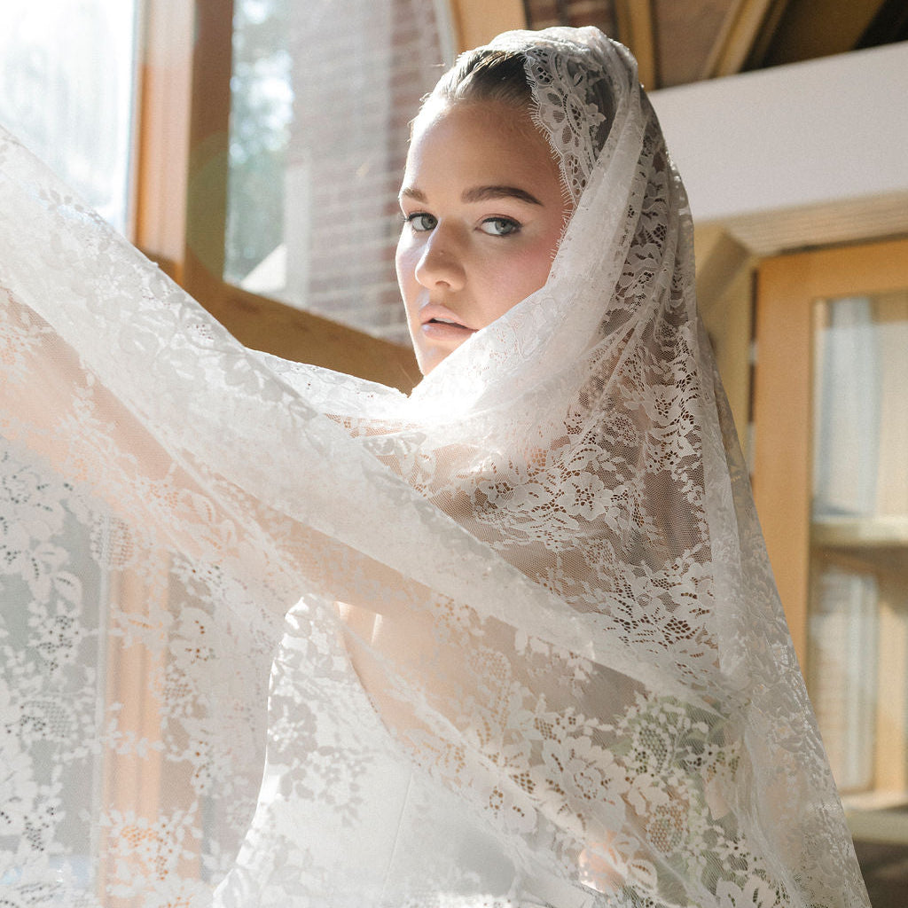 Woman wearing a lace veil indoors with a neutral background